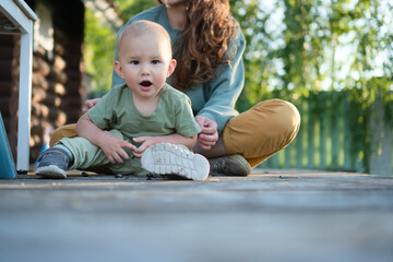 Content mother cuddles her smiling toddler amidst beautiful natural surroundings. Authentic moment of parental love and childhood wonder in the outdoors.