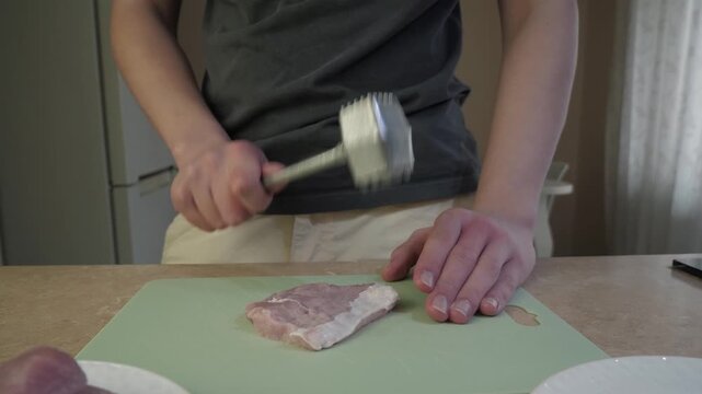 Pork tenderizing action, Home cook pounding pork meat, Closeup of hands flattening pork chop carefully, Casual kitchen scene showing hand tenderizing pork on cutting board