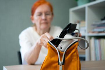 The blood pressure monitor is in sharp focus as a mature woman's hands take it from a protective case. Woman blurred in background. Emphasis on the product itself.