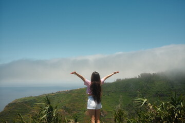 Fototapeta premium A wide shot of a young woman with arms open overlooking misty ocean landscape. Concept of solo traveling.