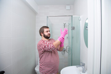 Photo. Long shot. Mature white fat man with beard, striped sweatshirt putting on pink rubber latex...