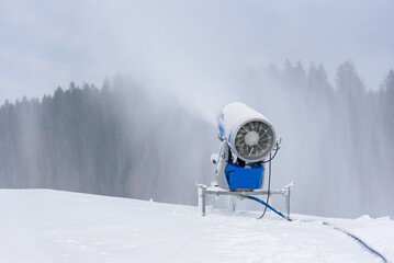Snow cannon spraying artificial snow on mountain ski slope