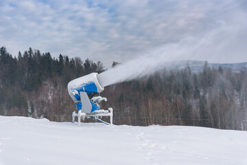 Snow cannon spraying artificial snow on mountain ski slope