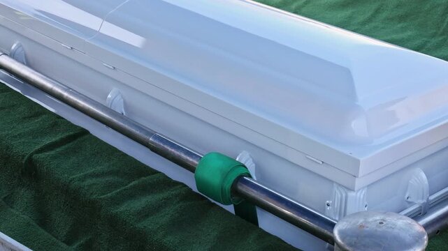 Casket on green grass at cemetery, surrounded by mourners burial during funeral ceremony.
