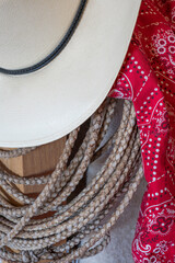 Closeup shows western gear, cowboy hat, rope rawhide lariat, and red bandana fabric.