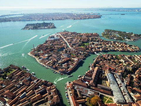 High altitude aerial view of Murano island with orange rooftops and canals, scenic panorama of Venice lagoon with Venice city skyline on the horizon, Italy.