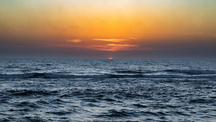 Sunset over the ocean, visible as a bright orange orb
