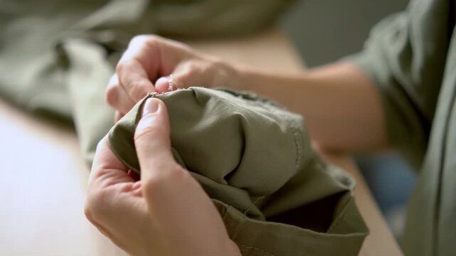 Close up of female hands carefully unpicking hem of pants. Sewing concept, repairing clothes, handmade hobby, useful skill. Woman working with needle, do it yourself tailoring project.
