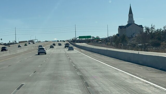 View from a truck cabin driving through Salt Lake City, Utah. Features the iconic church architecture on the right, city traffic ahead, and a clear sunny sky. Professional trucking workday.