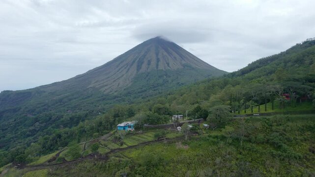 Cinematic aerial footage moving backward from Mount Inerie volcano peak, revealing lush green hills and local houses in Ngada, Flores, Indonesia.