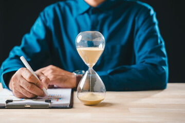 Hourglass displays time passing for busy business person diligently working on document management preparing vital financial reports meeting strict deadlines for job completion