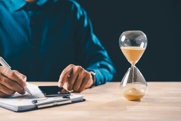Business professional focused on financial document analysis, hourglass time sand flowing indicating urgent deadline, work management crucial for busy project completion