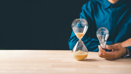 Hand holds clear lightbulb, sparking innovation idea for business growth, hourglass with flowing...