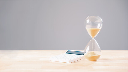 Hourglass shows time running out for tax day, calculator ready for business money, financial deadline approaching for income payment, corporate year end planning