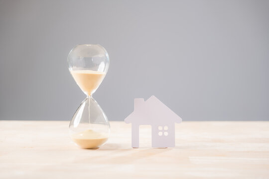 Hourglass, time, house, home, property, real estate mortgage concept visualizes sand flowing, showing need for investment loan money, temporary building buying selling accommodation - Powered by Adobe