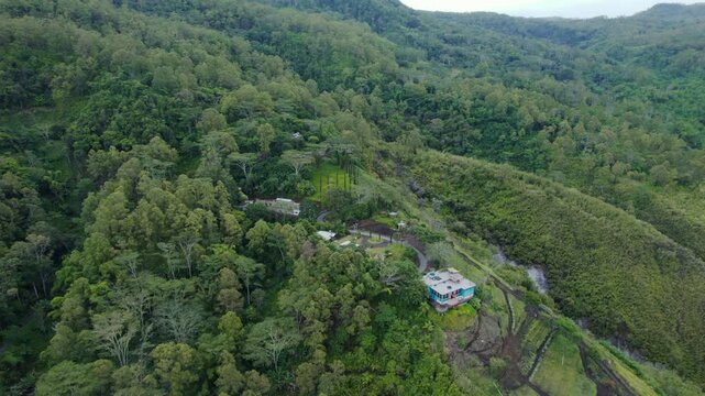 Cinematic drone shot of a lonely blue house nestled on a lush green hillside in the highlands of Bajawa, Flores, Indonesia.