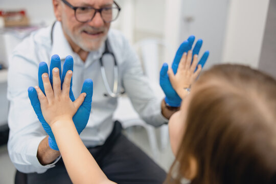 Male doctor doing high five with young girl inside exam room