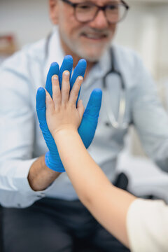 Male doctor doing high five with young girl inside exam room