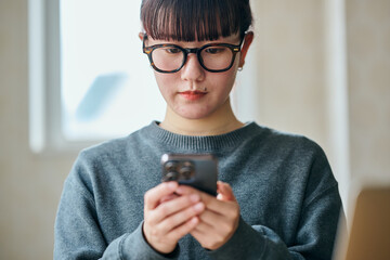 Young Asian woman wearing glasses using a smartphone for remote work communication