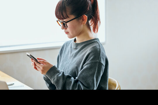 Young Asian woman wearing glasses using a smartphone for remote work communication - Powered by Adobe