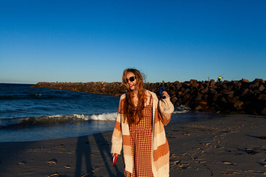 happy sunlit young woman at the beach with flying a kite holding onto reel with string to kite