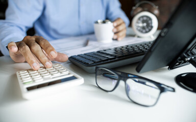 close up shot, accountant calculate business costs, profits and tax working with computer on desk checking financial documents and holding coffee cup during work