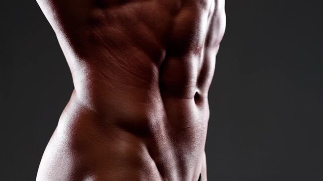 Close up of athletic torso with defined muscles against dark background