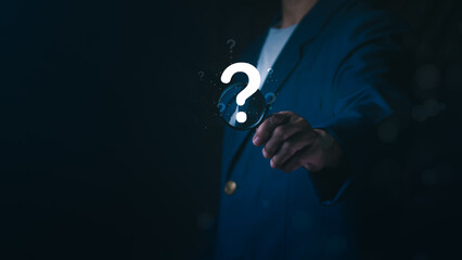 Businessman holding magnifying glass with glowing question mark icon, Concept of searching for answers, problem solving, market research, finding solutions, investigation, and business discovery.