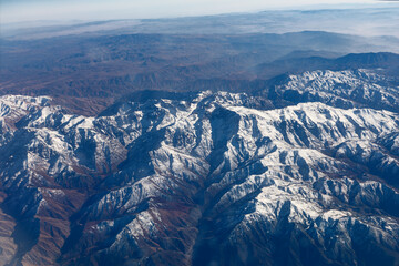 Atlas and Djurdjura ranges reveal dramatic relief, textures and vast North African wilderness. Aerial view of rugged mountain ridges with snow-capped peaks and deep valleys stretching to horizon