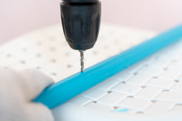 Close-up hand of man wearing cloth gloves and using a cordless drill to bore a hole a plastic (PVC) pipe.