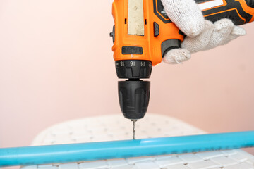 Close-up hand of man wearing cloth gloves and using a cordless drill to bore a hole a plastic (PVC) pipe.