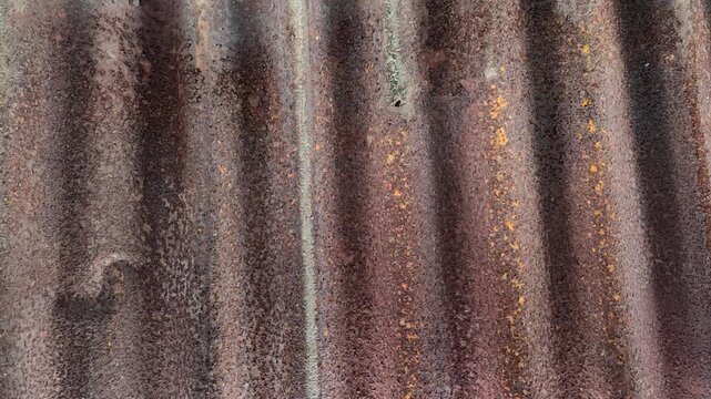 The texture of a rusted zinc roof with a vertical wavy pattern. The background of naturally corroded, aged metal gives an industrial, vintage, and grunge feel