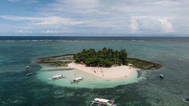 Tour boats anchored near sandy island with palm trees and clear blue Guyam Island. Siargao, Philippines.