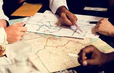 Business team planning strategic travel route on paper maps, hands drawing connections and logistics lines for exploration, transportation, geopolitics or corporate expansion project

