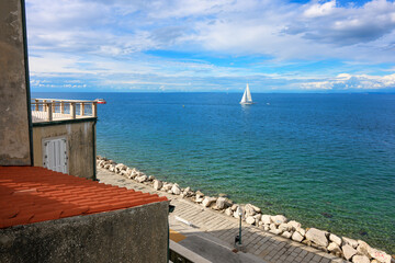A sailboat on the Adriatic Sea viewed from the rocky seaside promenade of Rovinj, Croatia, on the Istrian Peninsula.
