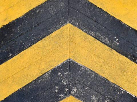 yellow and black chevron arrow pattern painted on a rough concrete surface - Powered by Adobe