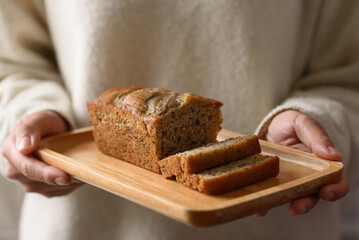 Delicious homemade banana bread or cake on rustic wooden plate holding by woman hand