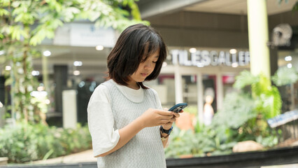 A young girl standing and looking at her smartphone in an indoor garden area.