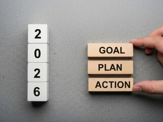 Hand placing action wooden block next to goal plan blocks and vertical stack of white 2026 number cubes showing resolution process