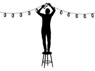 Man decorating with festive string lights on stool at night
