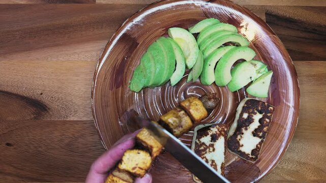 overhead view of person adding grilled chicharron on a plate with avocado and fried cheese