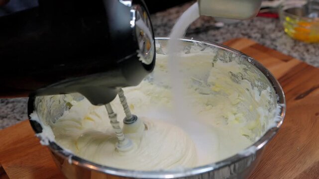 close up of pouring white granulated sugar into cheesecake batter while mixing with electric hand mixer