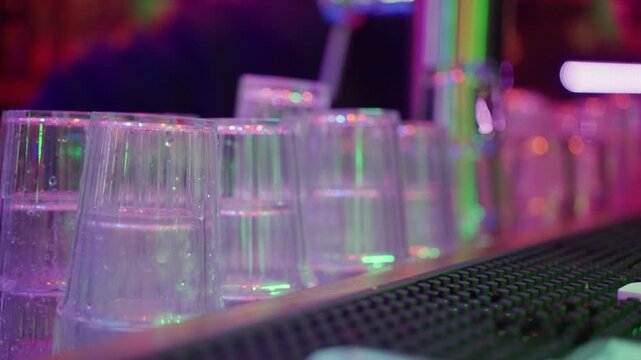 Neonlit Bar With Ready Cups, Colorful Neon Illumination Highlights Organized Rows Of Plastic Cups, Bright Neon Lights Illuminate Neat Stacks Of Transparent Cups Prepared For Lively Celebration