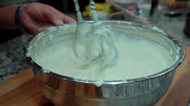 close up of electric hand mixer lifting out of smooth white cheesecake batter in a metal bowl