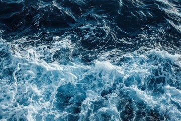 Naklejka premium A high-angle view of deep blue ocean water with white foamy waves crashing, creating a dynamic textured surface.