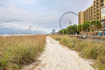 A wooden boardwalk seaside walkway along the dunes and sandy beach of the Atlantic Ocean with the skyline of Myrtle Beach, South Carolina in view. © Kirk Fisher