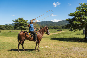 Costa Rican cowboy throwing lasso rope on horseback in green field