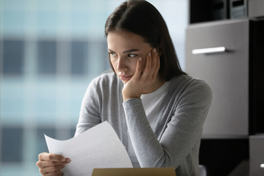 Nervous over letter. Stressed confused millennial businesswoman office worker student sit at desk prop head with hand think over paper document with bad project news declined offer failed agreement