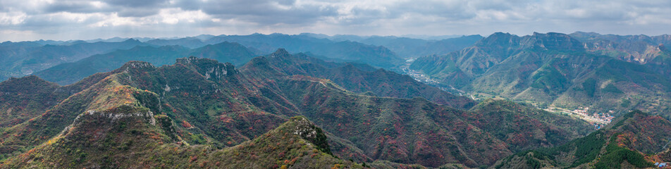 Naklejka premium Autumn red leaves blanket the mountains, creating a continuous layer of forest colors. The aerial view reveals a continuous range of layered mountain scenery