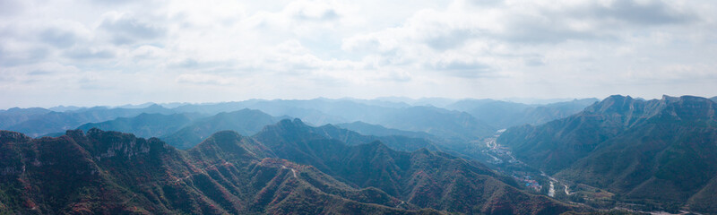 Fototapeta premium Autumn red leaves blanket the mountains, creating a continuous layer of forest colors. The aerial view reveals a continuous range of layered mountain scenery